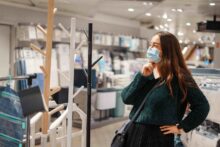 Девушка в медицинской маске в магазине рассматривает декоративные вешалки для одежды.
